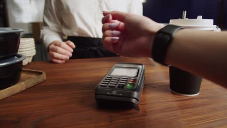 paying with smartwatch in cafe. contactless, touch-free shopping in pubs. nfc technology concept, using fitness bracelet payment via terminal close-up.