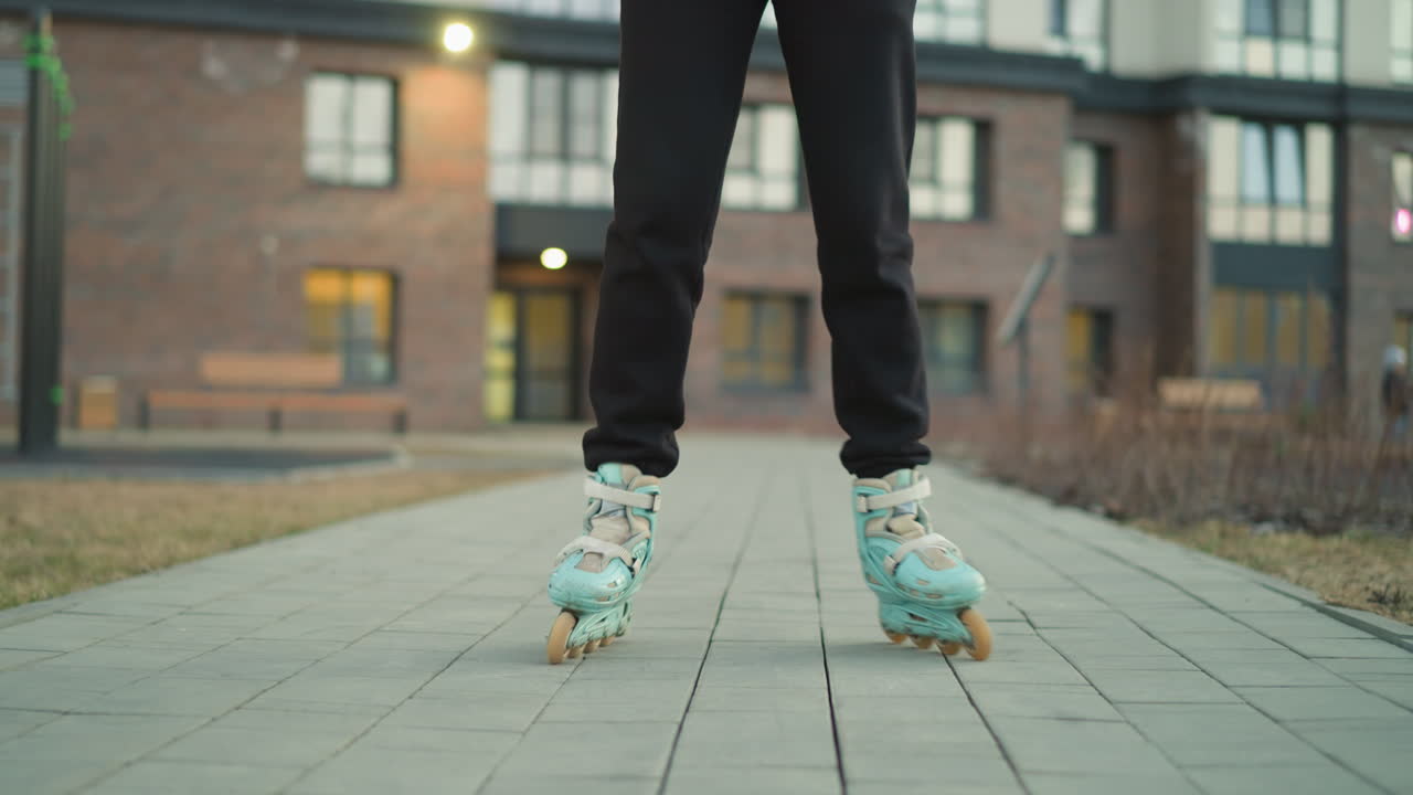 Front shot the motion of rollerblades as they glide smoothly over a paved path in a park. Residential buildings are visible in the background, showcasing the urban environment and outdoor activity