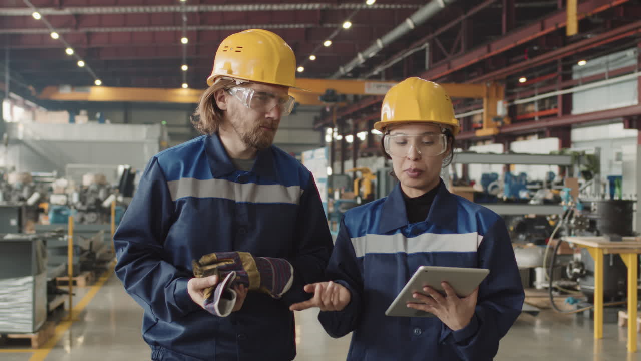 Couple Of Factory Workers With Tablet Walking Through Plant Facility