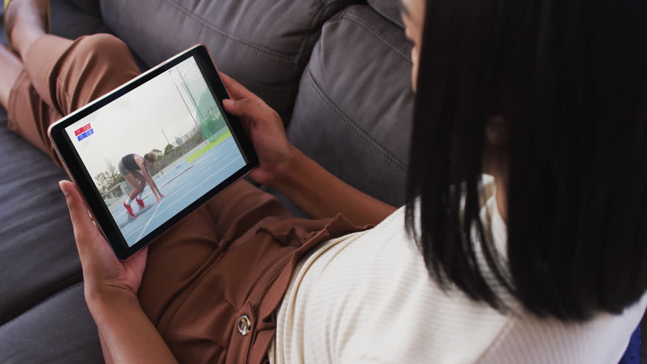 Composite of woman sitting at home on couch watching athletics running event on tablet