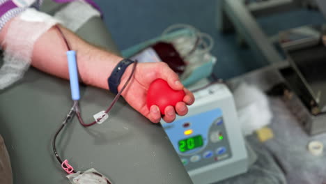 little red rubber heart in the hand of a male donor. catheter is filled with blood. transfusion and donation of blood.