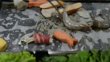 cooking shrimps and mixed processed meats in a hot pan with little amount of oil - closeup shot