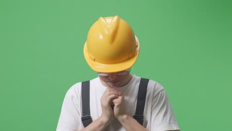 close up of asian man worker wearing goggles and safety helmet praying for something while standing in the green screen background studio