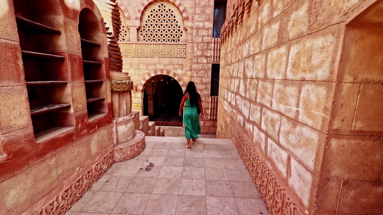 Rearview follows woman in flowing dress walk between traditional buildings in Sharm El Sheikh, Egypt