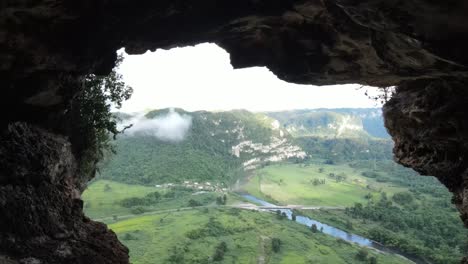 view from rocky cave on green forested valley and river