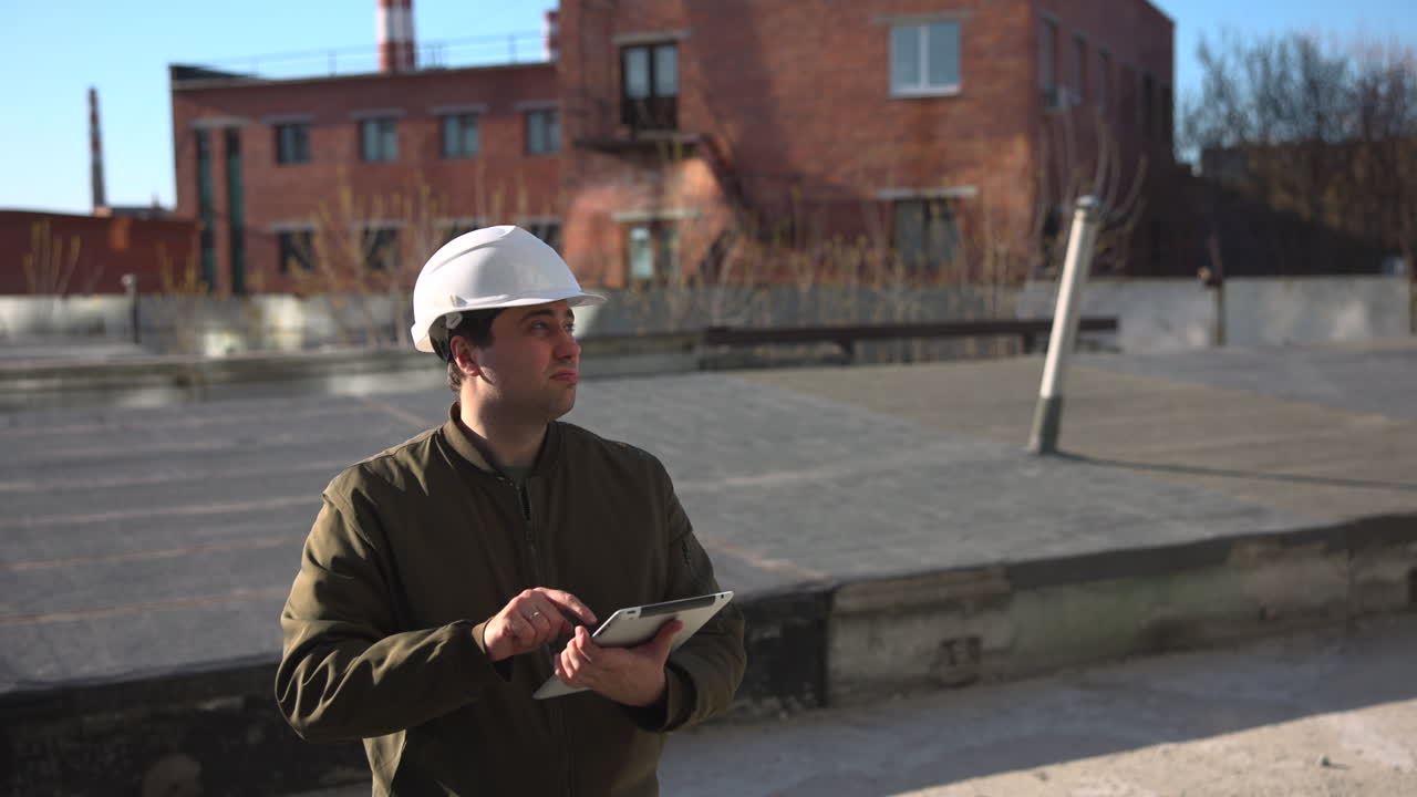 Caucasian Site Surveyor Using Tablet On Rooftop Construction Site In Daylight, White Helmet, Brick Building