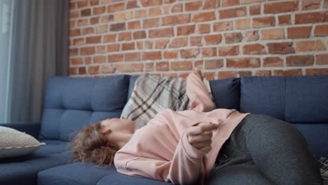 Tracking-video-of-caucasian-young-woman-lying-down-on-sofa-and-covering-with-a-blanket.