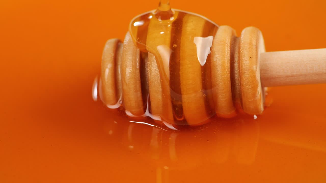 Miele che cola su un mestolo per miele su sfondo giallo. Primo piano di miele denso, biologico e sano. Dolce al miele 4K