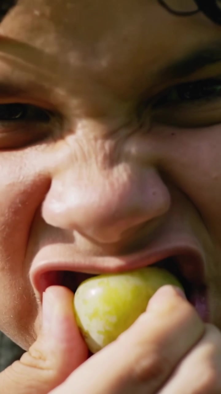 Vertical video: Lifting teen holding green fruit to mouth in garden chewing and testing flavor
