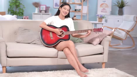 young cute girl sitting cross-legged on the sofa enjoyed playing guitar