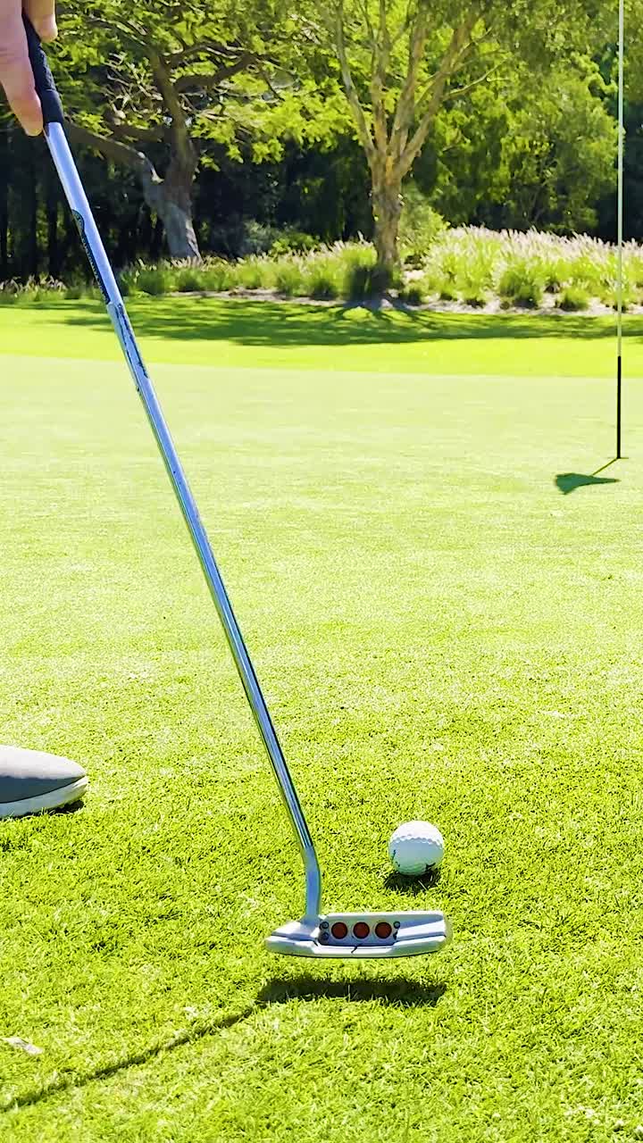 A golfer putts a white ball across a lush green towards a distant flag