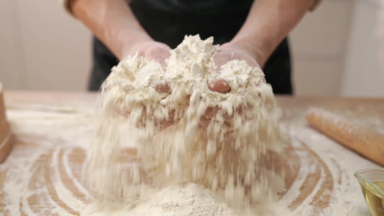 Primo piano di mani che setacciano la farina su un tavolo di legno al rallentatore