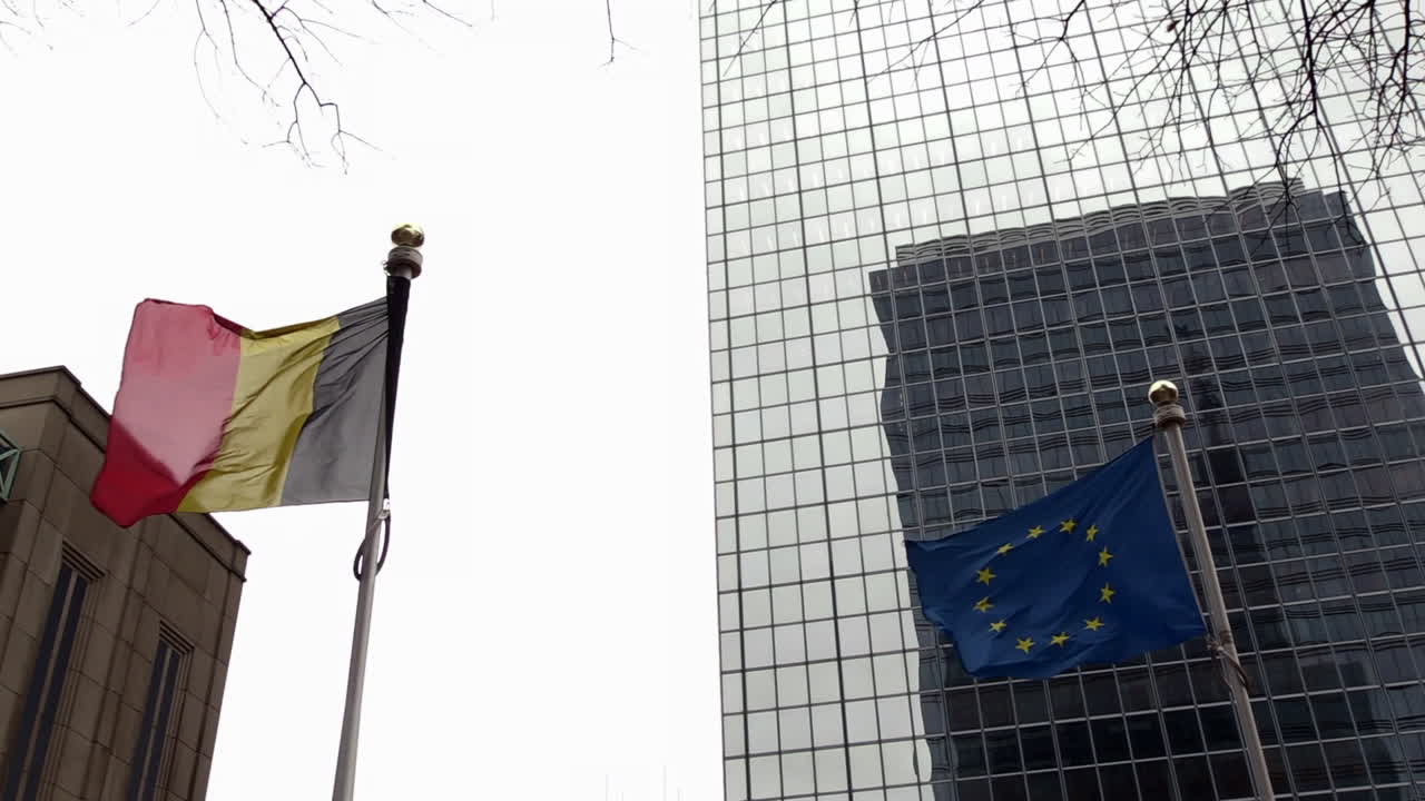 Una bandiera belga e una europea che sventolano al vento in una giornata nuvolosa davanti a un edificio a Bruxelles.