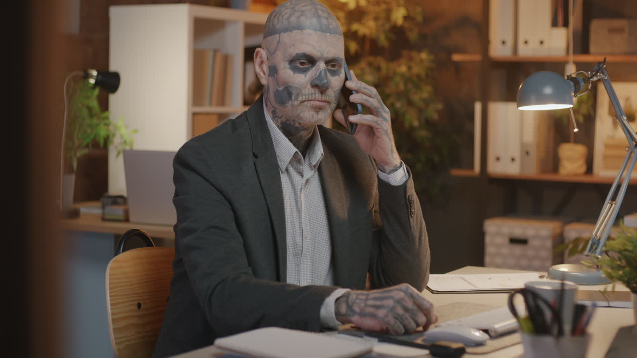 Businessman with Skull Tattoo on Face Talking on Phone in Office