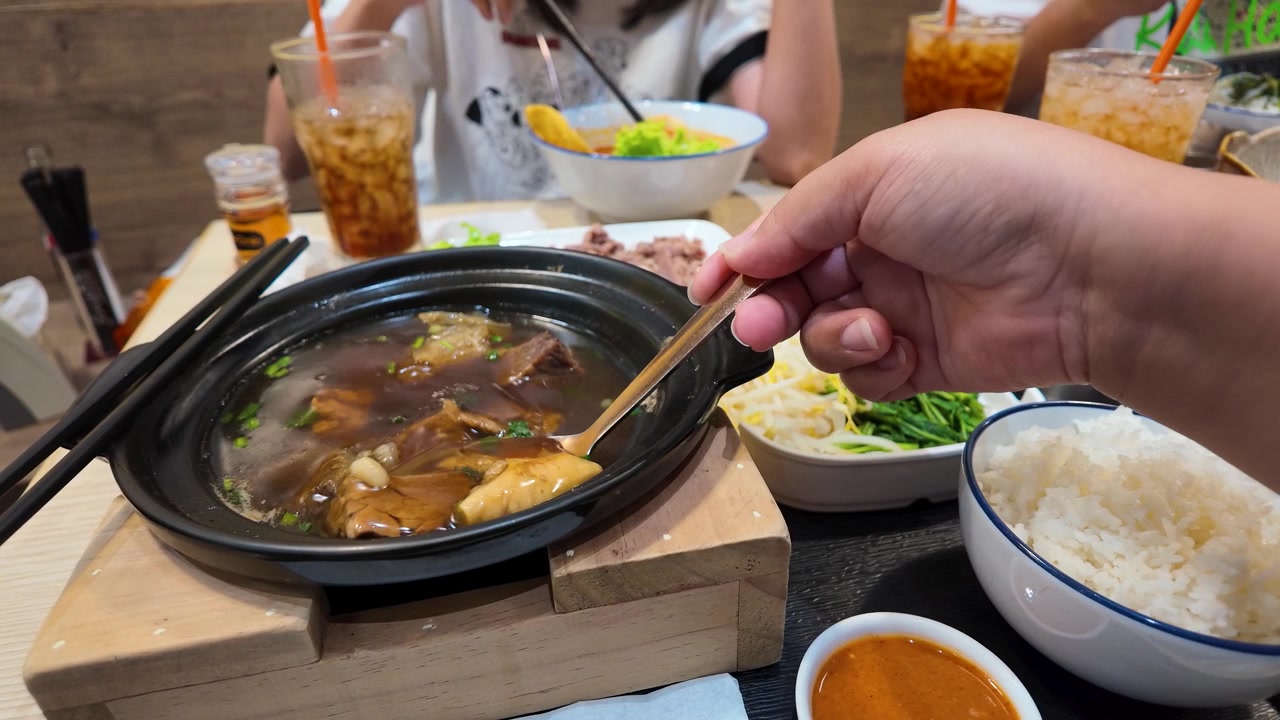 Close-up tangan menggunakan sendok untuk makan semur daging sapi panas di Bangkok, Thailand.