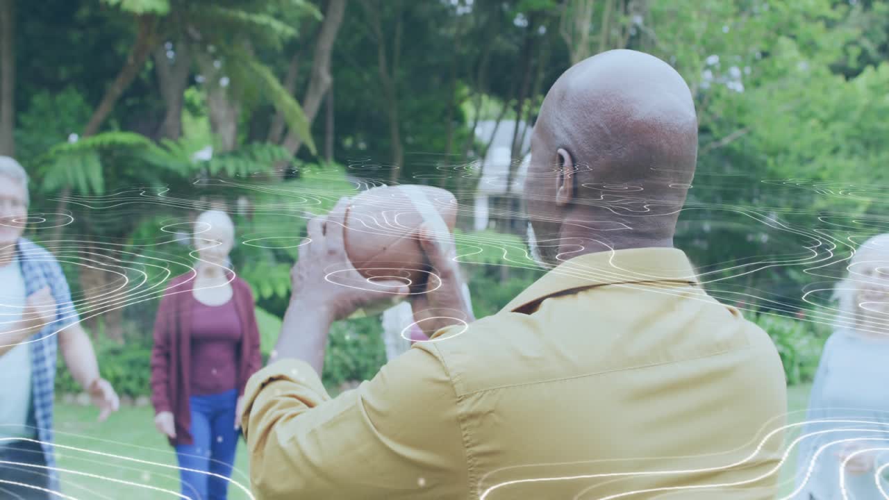 Senior man raising arm and tossing football in fitness-themed backyard session, engaging friends