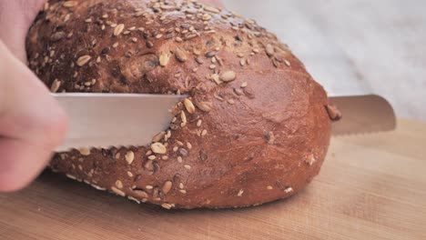 A-man-cuts-freshly-baked-bread-covered-with-seeds-with-a-knife-on-a-wooden-board