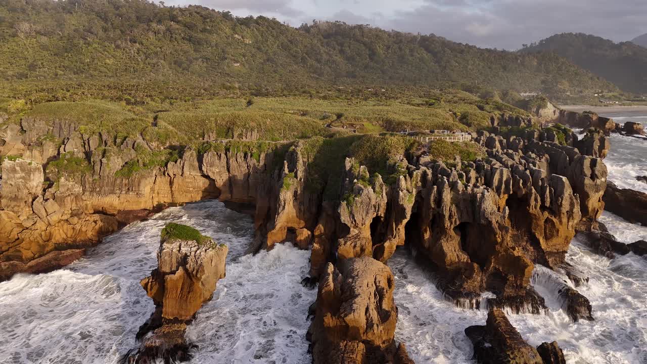 Vista aerea con drone di potenti onde oceaniche che si infrangono contro le uniche formazioni calcaree delle Pancake Rocks al tramonto a Punakaiki, Nuova Zelanda.