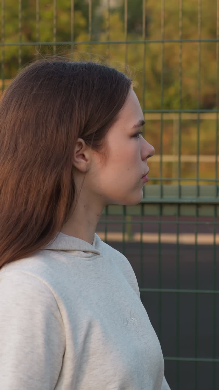 una mujer pasa por la valla del estadio sola al atardecer. una mujer joven mira con tristeza el campo de deportes pensando en el miedo al fracaso. luchando contra las preocupaciones internas
