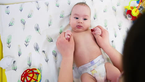 surgeon moves baby's hands back and forth. child is staying calm and watching the doctor with curiosity. view from above.