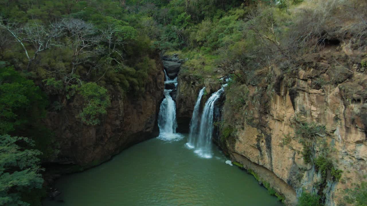 As cachoeiras de Turbinas Santa Cruz desaguam em uma piscina circular verde rodeada por florestas e penhascos, afastamento da câmera do drone para uma vista panorâmica, Jalisco, México