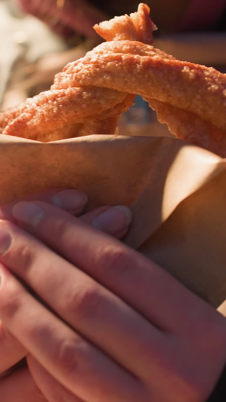 primer plano de una persona sosteniendo un delicioso bocadillo en la mano, iluminado por una luz suave, mostrando giros dorados de pasteles envueltos en papel en un parque de invierno al aire libre