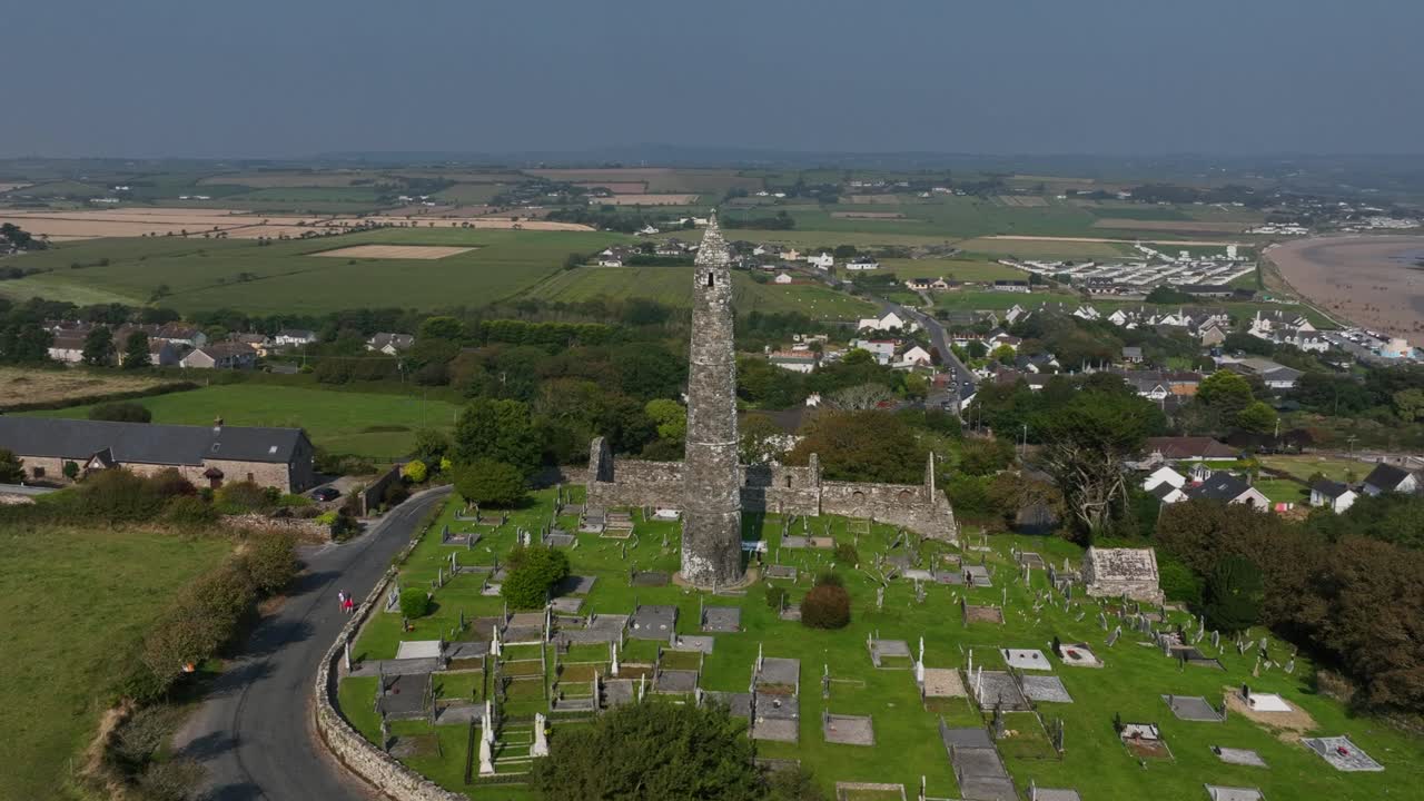 St. Declan's Monastery, Ardmore, County Waterford, Ireland, September 2024. Drone orbits clockwise above the graveyard and Cathedral ruins as blue ocean waves crash against the beach in the distance.