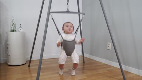 the beautiful baby having a great time jumping in a special bouncer made from a metal frame and hanging spring