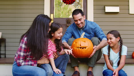 retrato de una familia con una calabaza de halloween tallada en los escalones de la casa