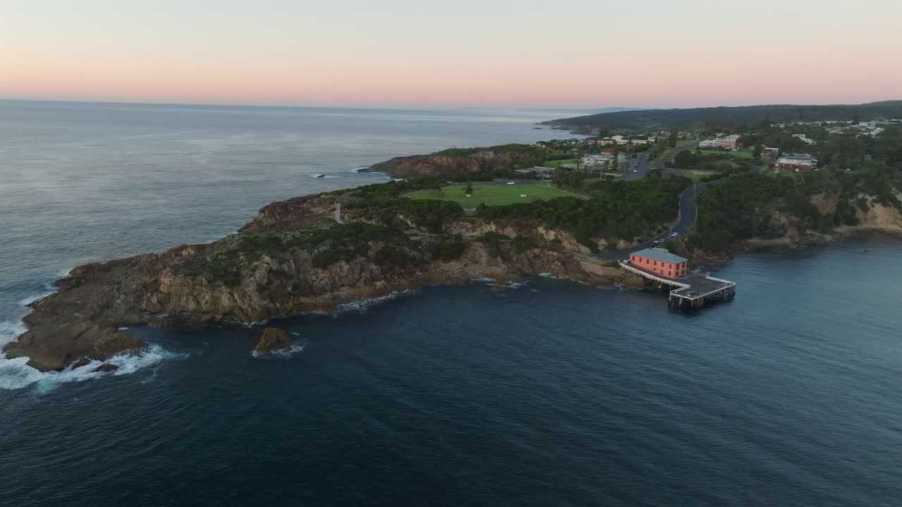 Aerial: Drone slowly tracking around Tathra Wharf and headland during early morning dawn, South Coast NSW, Australia