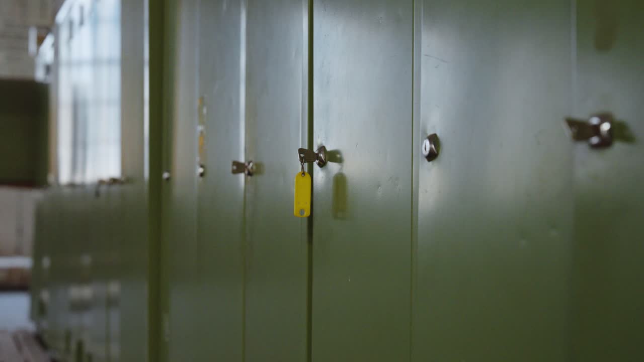 Slow camera dolly back past green lockers with key in focus – moody industrial setting