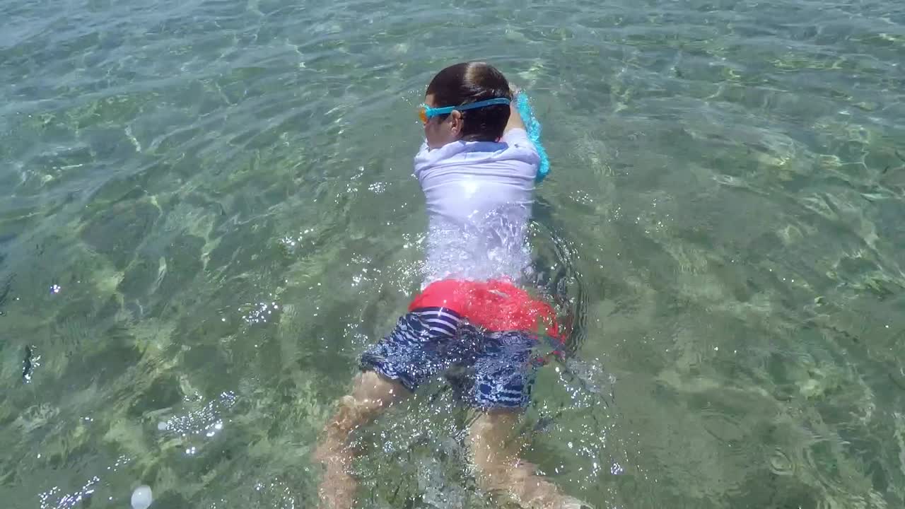 백인 아이는 맑은 바닷물을 즐기고 수영 보드에서 쉬고 있습니다.