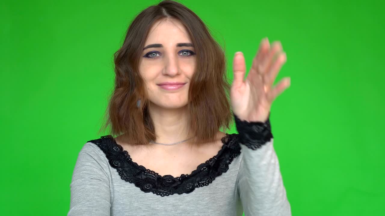 Young woman raising hand while looking at the camera over green background.