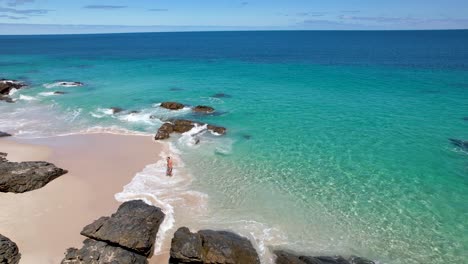una pareja caminando fuera de un océano azul brillante a una playa de arena blanca