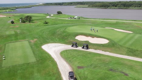 sweeping drone view of a green, scenic coastal golf course on a sunny day with players and carts