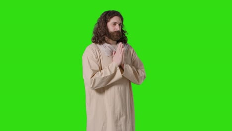 tomada de estudio de un hombre vestido con túnicas con cabello largo y barba que representa la figura de jesucristo orando en la pantalla verde 1