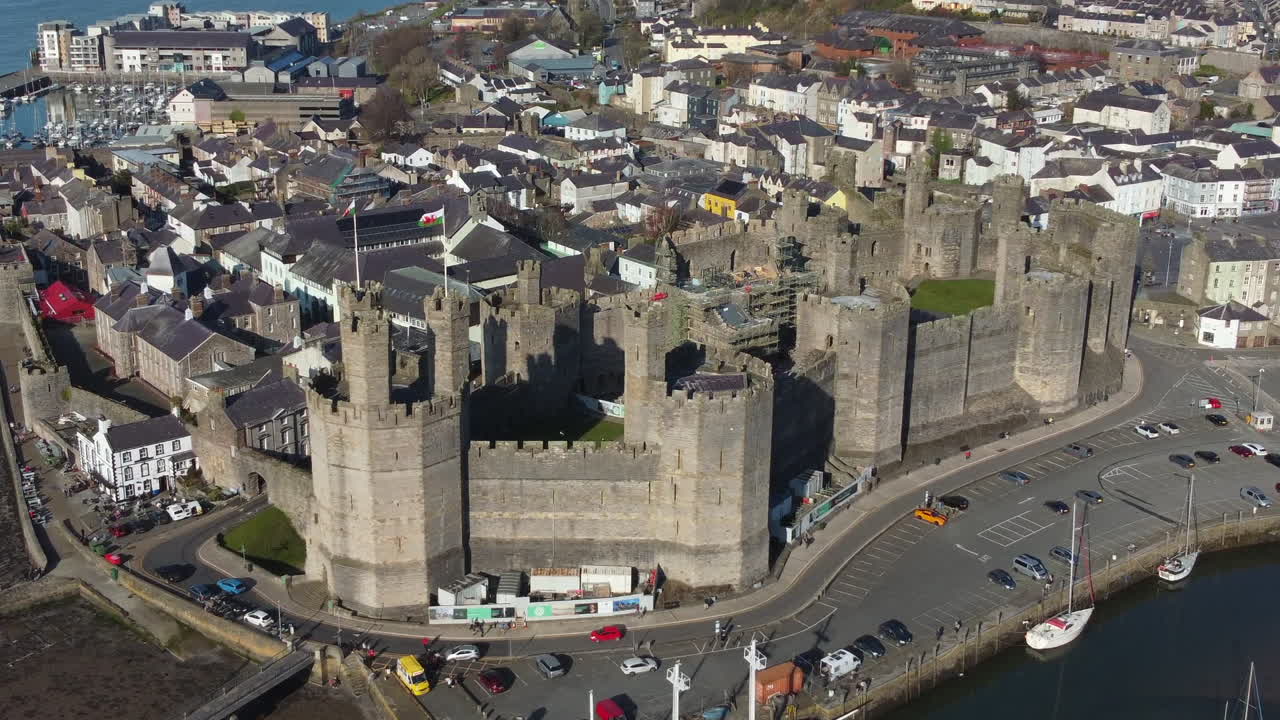 Una vista aerea del Castello di Caernarfon in una giornata di sole, volando da destra a sinistra intorno al castello mentre si zooma indietro, Gwynedd, Galles del Nord, Regno Unito