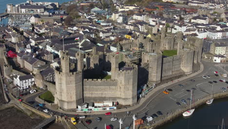 an aerial view of caernarfon castle on a sunny day, flying right to left around the castle while zooming out, gwynedd, north wales, uk