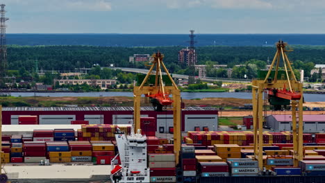 massive cranes load colorful shipping containers at the freeport of riga with forested backdrop. riga, latvia