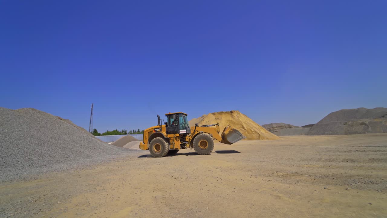 Excavator moving among piles of gravel. Asphalt plant. Industrial machinery working outdoors.