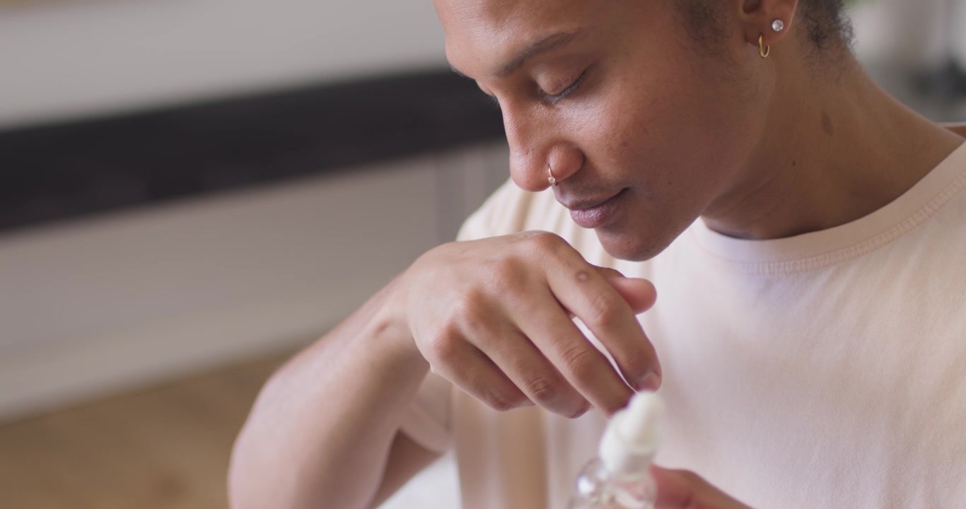 African American man opening dropper drawing oil applying to hand smelling to test at spa table