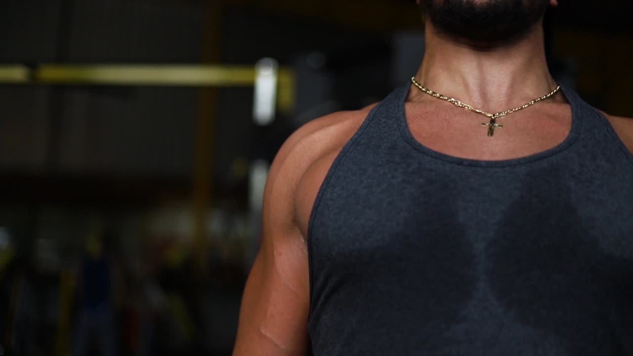 joven caucásico barbudo fuerte que usa cruz sacude los músculos del pecho levantando peso muerto pesado en el gimnasio, cierra el retrato a cámara lenta