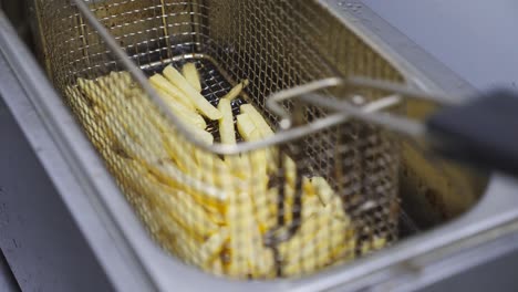 mano masculina del cocinero sacudiendo una rejilla con papas fritas que se preparan en aceite hirviendo caliente. brazo del chef bajando una cuadrícula con patatas en la freidora profunda. proceso de hacer comida rápida en la cocina. vista superior