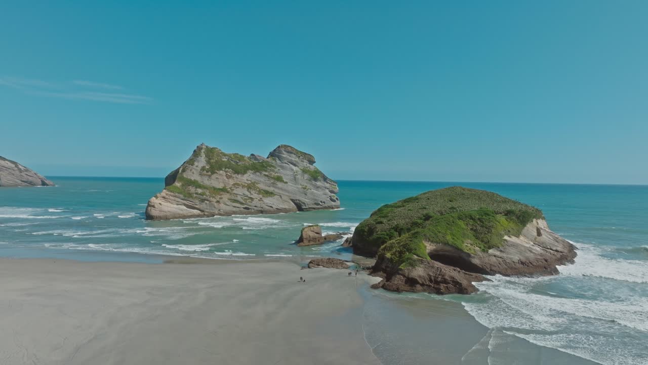 Aerial view of tourist visiting popular destination of Wharariki Beach with unique rocky outcrops in the Tasman Sea at Cape Farewell, South Island of New Zealand Aotearoa