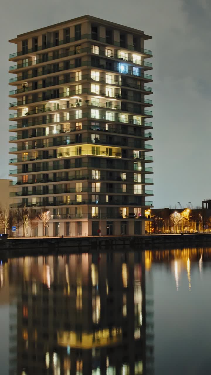 Panning night timelapse of lit high-rise apartments reflected in calm waterfront