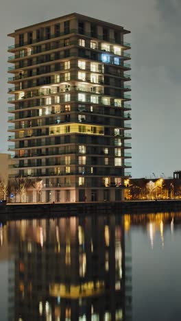 panning night timelapse of lit high-rise apartments reflected in calm waterfront