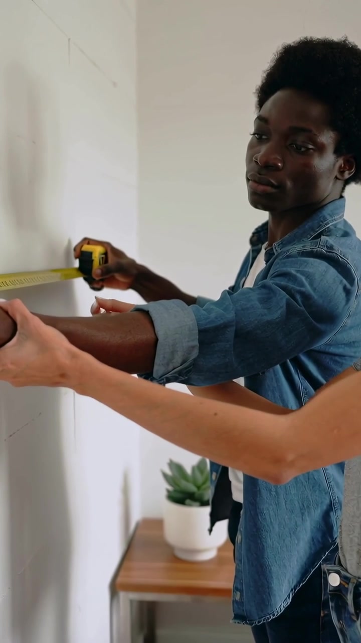 Vertical video: Holding tape against wall, man and woman measuring for marking at home in denim