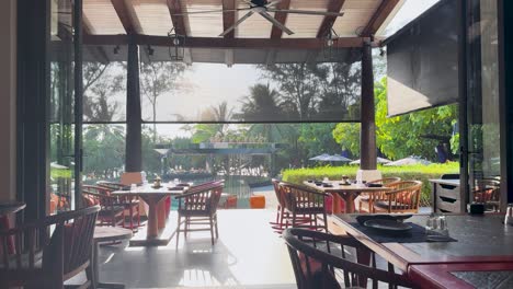 empty resort dining area with wooden furniture, natural light, and lush greenery in phuket, thailand. calm and inviting atmosphere