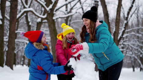 family playing and building a snowman in a snowy park