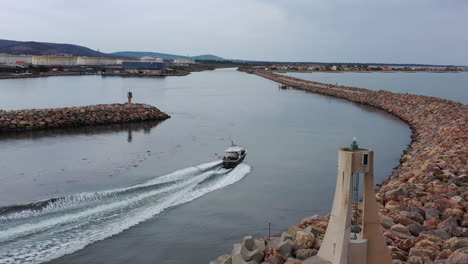 boat entering a canal aerial drone shot lighthouse and breakwater along france